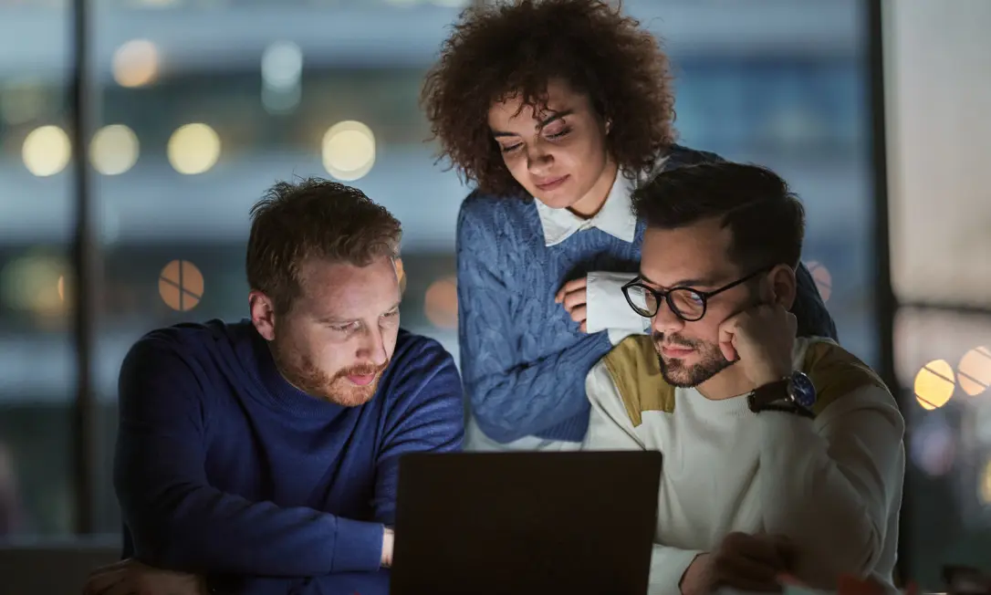 Three employees collaborate around a computer, browser activity secured by Dashlane’s AI phishing alerts